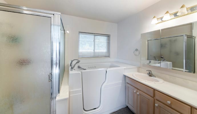A full view of an accessible bathroom featuring a walk-in tub set in a custom deck, a separate shower stall, and a vanity with a large mirror.