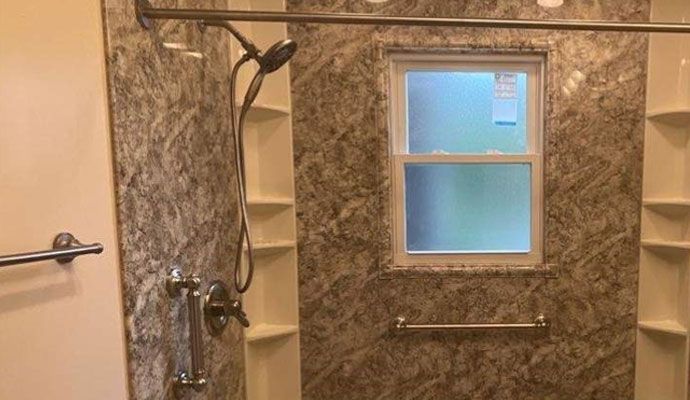 A remodeled shower featuring a modern handheld shower wand, granite-patterned wall panels, and a window inside the enclosure.