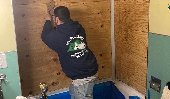 A remodeling contractor from Mt. Pleasant Remodeling is installing plywood panels on the walls of a shower enclosure during a bathroom renovation.