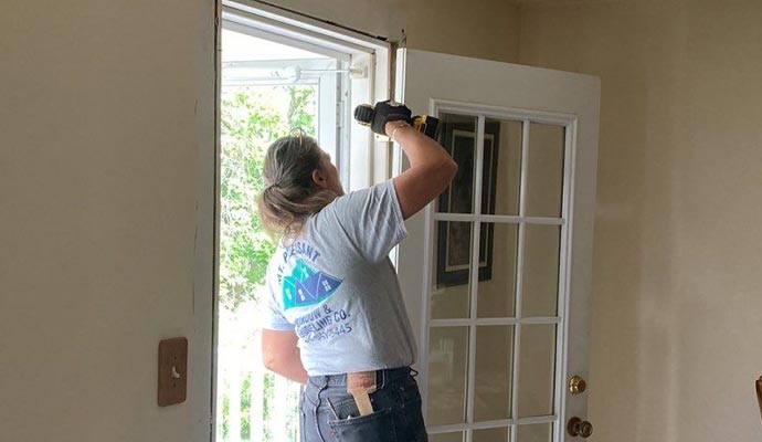 Professional Door Installation Service A female contractor from Mt. Pleasant Window & Remodeling Co. uses a power drill to install a white French patio door.